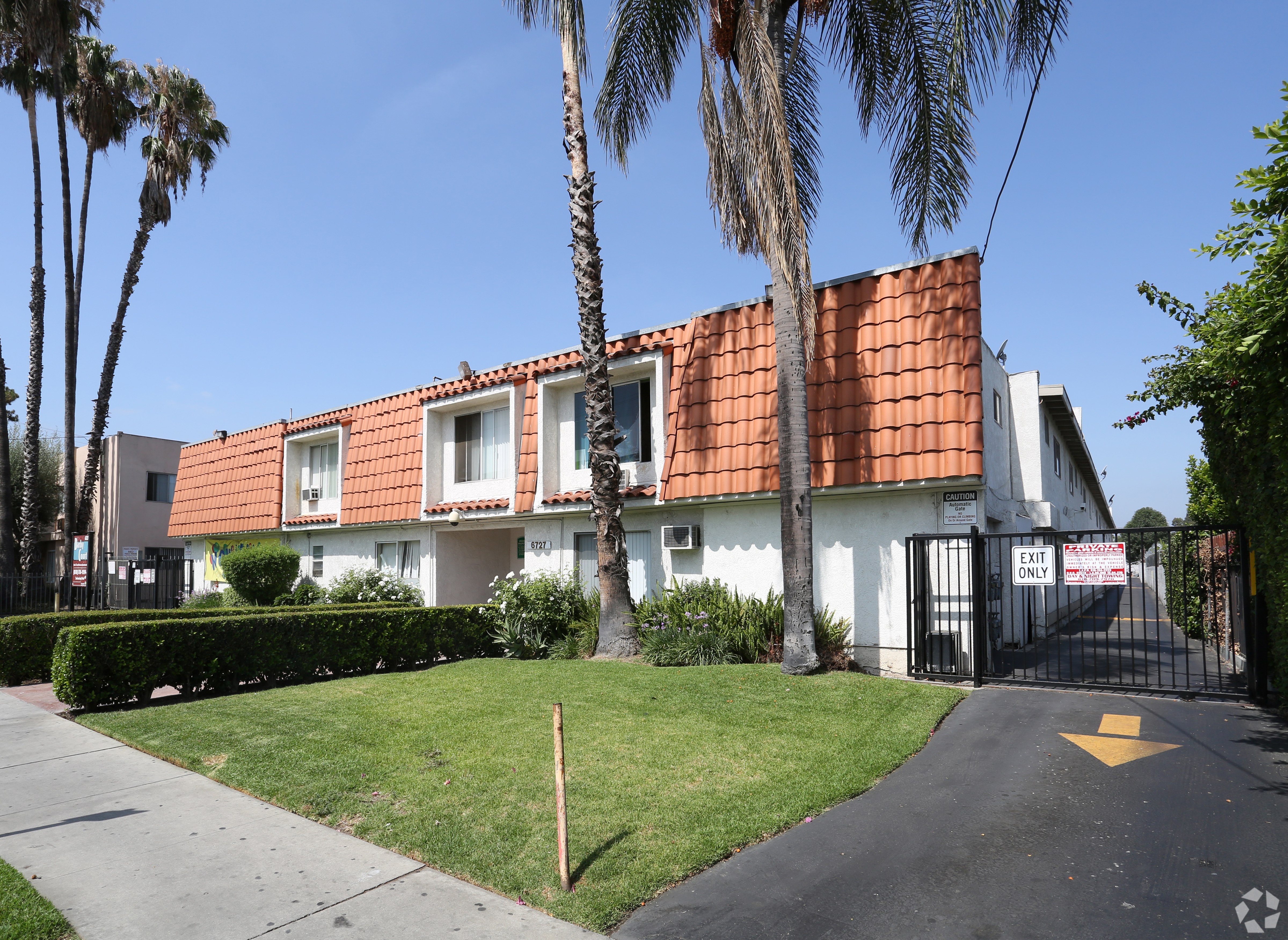 A white house with a red tile roof is surrounded by palm trees.